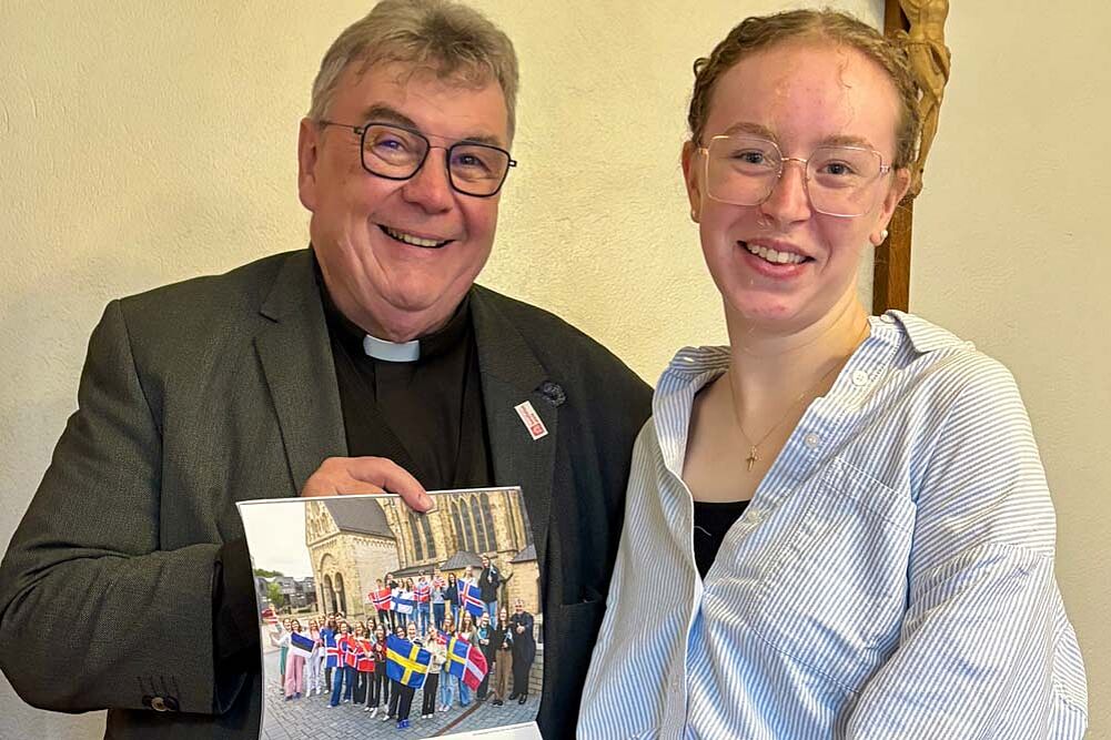 Monsignore Gerog Austen überreicht „Praktikantin im Norden“ Luisa Maas ein druckfrisches Exemplar des Bonifatiuswerk-Kalenders. Er zeigt ein Foto aller Teilnehmer des Freiwilligen-Programms 2025. Foto: privat