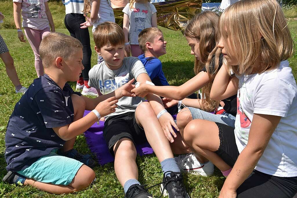 Theo (6) und Julia (8) üben an Jonathans Arm, wie man am besten einen Verband anlegt. (Foto: Simon Helmers)