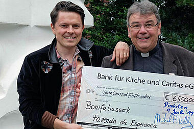 Michael Patrick Kelly und Monsignore Georg Austen bei der Scheckübergabe. Mit den 6.500 Euro unterstützt das Bonifatiuswerk die „Fazenda da Esperança“, ein Wohnprojekt für ehemalige Drogen- und Alkoholabhängige in Nauen in Brandenburg.