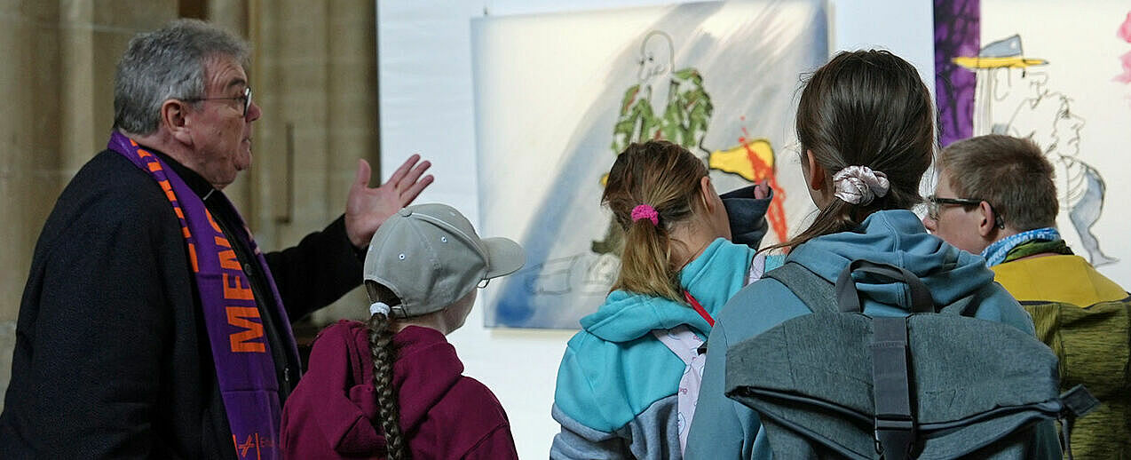 Monsignore Georg Austen, Generalsekretär des Bonifatiuswerkes, erklärt jungen Besuchern einige Werke der Ausstellung "Udos 10 Gebote". Foto: Pia Wittek