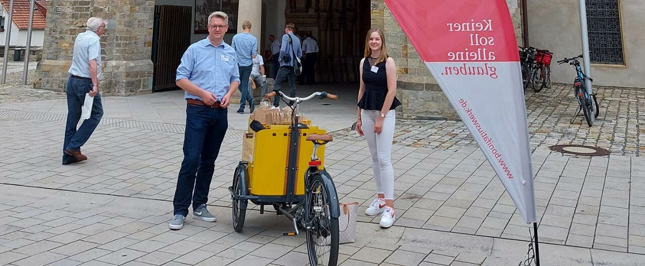 Thomas Twents, Bereichsleiter Projektverwaltung und Verkehrshilfe beim Bonifatiuswerk, und Bundesfreiwilligendienstlerin Theresa Brautmeier mit dem Boni-Bike auf dem Domvorplatz (Foto: Katrin Sijbom)