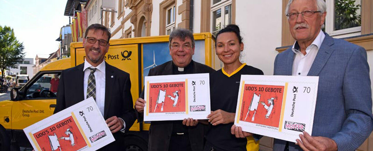 So wird die neue BRIEFMARKE INDIVIDUELL aussehen: Von Links: Uwe Scholle (Vertriebsmanager Deutsche Post), Monsignore Georg Austen (Generalsekretär des Bonifatiuswerkes), Maria Miskowiec (Zustellerin Deutsche Post) und Heinz Paus (Präsident des Bonifatiuswerkes) zeigen die neue Briefmarke zur Ausstellung „Udos 10 Gebote“. Foto: Patrick Kleibold