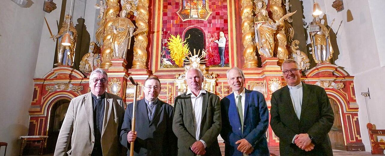 Monsignore Georg Austen (links), Pfarrdechant Dr. Hans-Bernd Krismanek, Künstler Thomas Jessen, Professor Dr. Christoph Stiegemann und Generalvikar Monsignore Dr. Michael Bredeck vor dem neuen Hochaltargemälde. Es ist zum Themenabend glanzvoll ausgeleuchtet worden. Der Pilgerstab, den Monsignore Austen dem Pfarrdechanten überreichte, unterstreicht ebenso wie das Hochaltarbild die enge Verbundenheit zwischen dem Bonifatiuswerk und Corvey. (Foto: Kirchengemeinde Corvey/Sabine Robrecht)