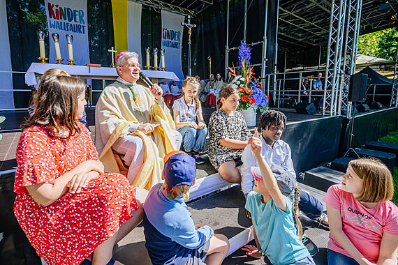 Erzbischof Dr. Udo Markus Bentz führt mit einigen Kindern ein Predigtgespräch auf den Stufen der Altar-Bühne. Foto: Besim Mazhiqi / Erzbistum Paderborn
