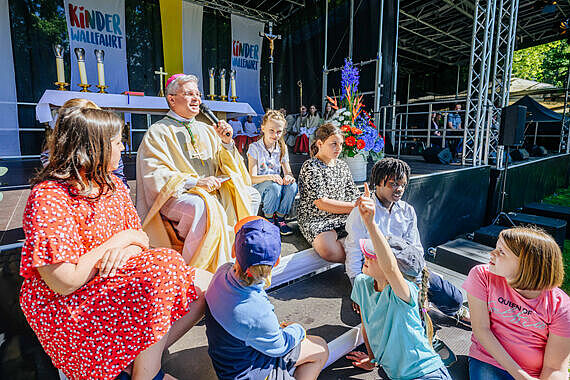 Erzbischof Dr. Udo Markus Bentz führt mit einigen Kindern ein Predigtgespräch auf den Stufen der Altar-Bühne. Foto: Besim Mazhiqi / Erzbistum Paderborn