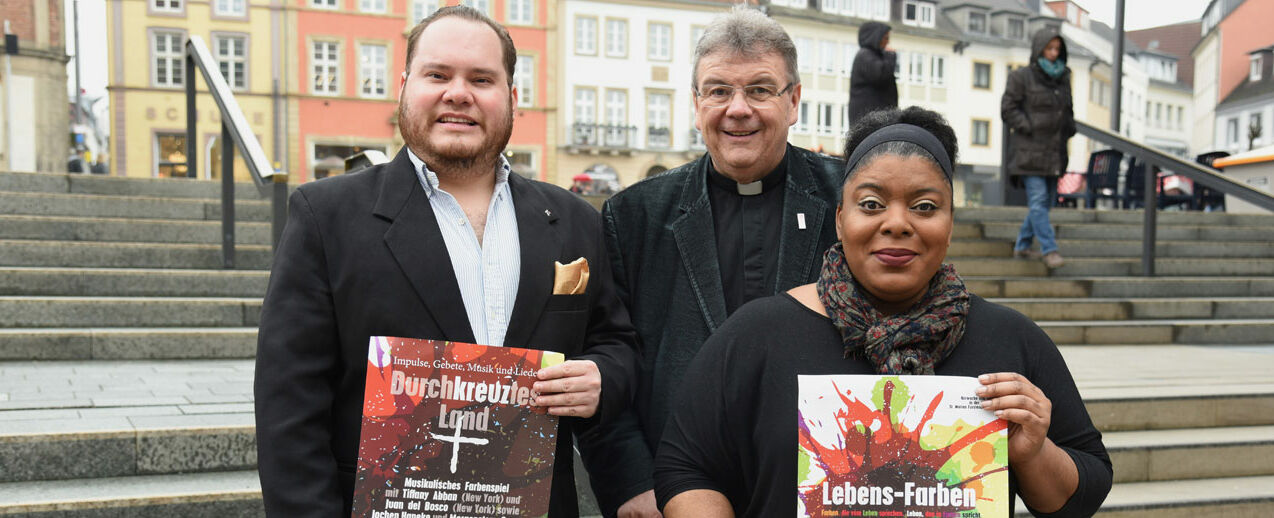 Juan Del Bosco (links), Tiffany Abban und Monsignore Georg Austen präsentieren die Plakate zum Programm für die Kar- und Ostertage in Fürstenberg, Büren, Leiberg und Paderborn. Foto: Sr. Theresita