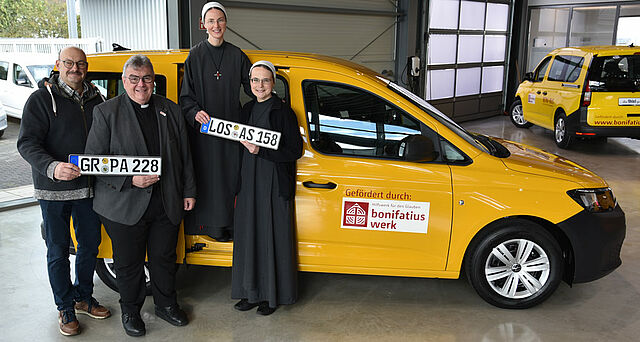 Dietmar Pohl (links) vom Ordinariat Görlitz sowie Schwester M. Lioba und Schwester M. Gloria (von rechts) von der Neuzeller Schwesterngemeinschaft Dienerinnen vom Heiligen Blut nahmen von Monsignore Georg Austen jeweils einen BONI-Bus-Caddy entgegen. (Foto: Simon Helmers)