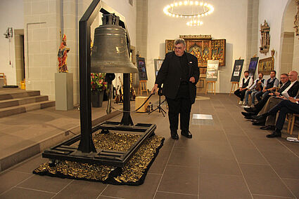 Monsignore Georg Austen, Generalsekretär des Bonifatiuswerkes, läutet die #PeaceBell zur Eröffnung der Ausstellung in der Gaukirche am Freitagabend. Am kommenden Mittwoch ist der Künstler Michael Patrick Kelly bei einem internationalen Friedensgebet im Paderborner Dom selbst zu Gast. (Foto: Matthias Band)