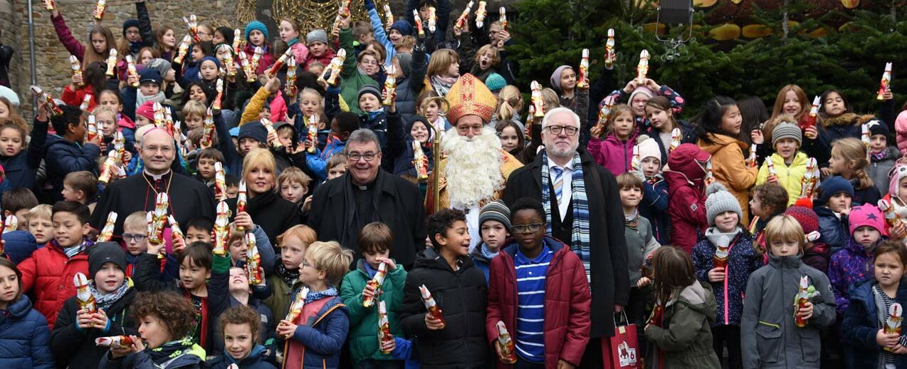 Die Schokonikoläuse kommen bei den Schülern der Domsingschule gut an. Gruppenbild mit Bischof Dieser, Maite Kelly, Msgr. Georg Austen, Bischof Nikolaus und Bürgermeister Plum (v.l.) (Foto: Theresa Meier)