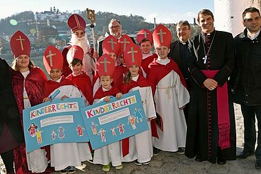 Acht Kinderbischöfe aus der Grund- und Mittelschule St. Nikola in Passau haben gemeinsam mit dem heiligen Nikolaus, Maite Kelly (links), Passaus Oberbürgermeister Jürgen Dupper (Mitten hinten), Monsignore Georg Austen (dritter von links), Bischof Stefan Oster und dem stellvertretenden Landrat, Raimund Kneidinger, die Weihnachtsmannfreie Zone des Bonifatiuswerkes in Passau eröffnet. Foto: Patrick Kleibold