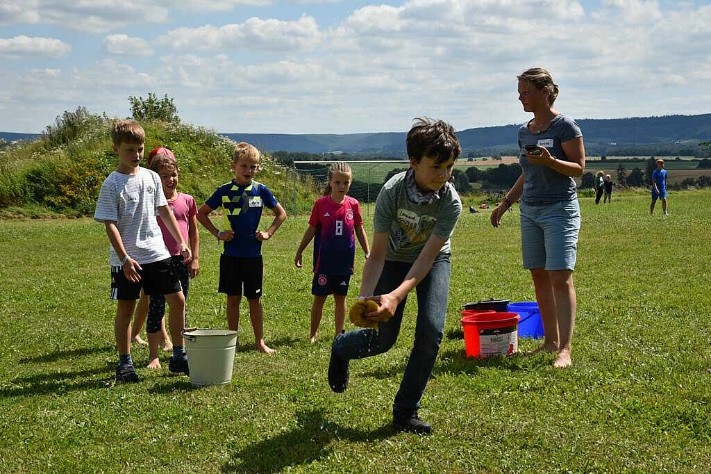 Kerstin Werner (rechts) stoppt die Zeit, während die Kinder das Wasser von einem Eimer zum anderen transportieren. Gerade läuft Leonard (12) mit dem Schwamm. (Foto: Simon Helmers)