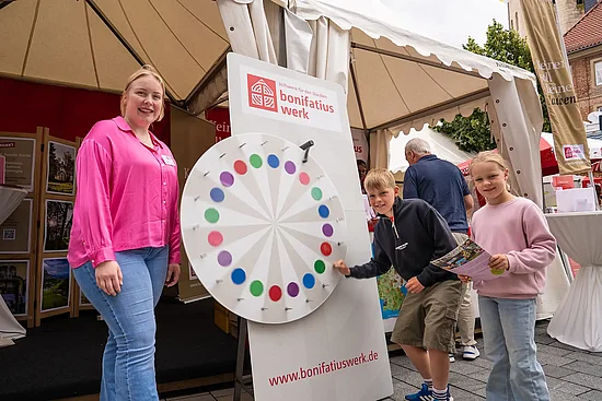 Leo (10) aus Paderborn hängt sich beim Glücksrad voll rein. Mit im Bild: seine Schwester Leni (7) und Alena Lorenz (Bonifatiuswerk). Foto: Hartmut Salzmann