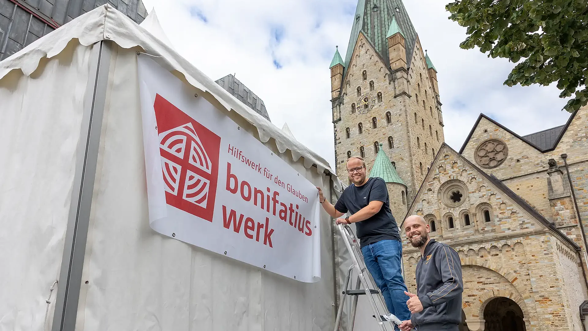 Julian Heese (Bereichsleiter Missionarische und diakonische Pastoral, li.) und Sachbearbeiter Sebastian Müller legen am Bonifatiuswerk-Infostand letzte Hand an. Foto: Hartmut Salzmann