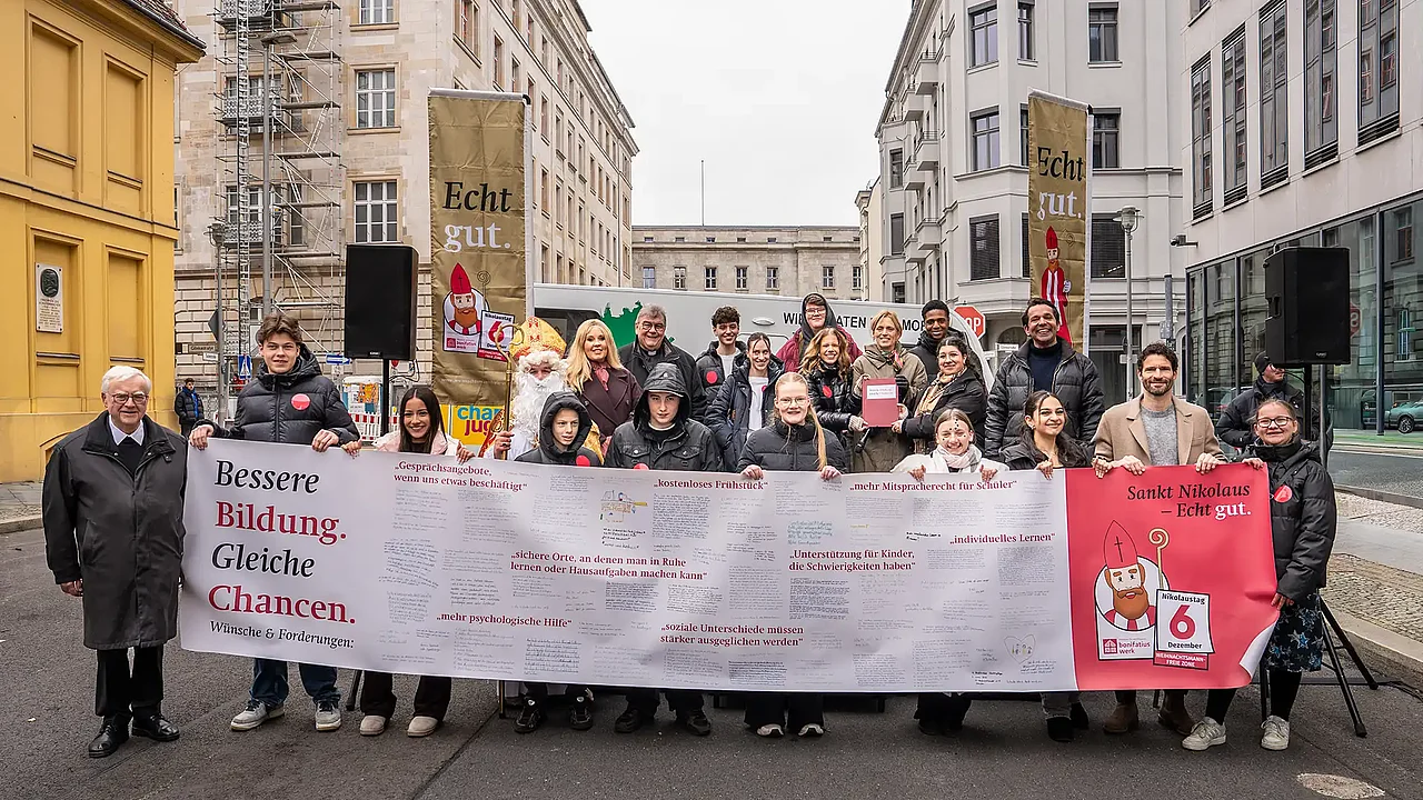 Höhepunkt der bundesweiten Nikolausaktion des Bonifatiuswerkes in Berlin: Auf einem fünf Meter langen Banner überreichten Jugendliche ihre Forderungen für bessere Bildung und gleiche Chancen an Bundesjugendministerin Karin Prien (letzte Reihe mit Buch). Mit im Bild: Maite Kelly (Botschafterin der Nikolausaktion, hintere Reihe 2.v.l.), Bonifatiuswerk-Generalsekretär Monsignore Georg Austen (hintere Reihe 3.v.l.), Erzbischof Dr. Heiner Koch (links), Ex-Fußballprofi und Stiftungsgründer Arne Friedrich (2. v.r.) und Moderator Juri Tetzlaff (3. v.r.). Foto: Hartmut Salzmann