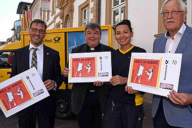 So wird die neue BRIEFMARKE INDIVIDUELL aussehen: Von Links: Uwe Scholle (Vertriebsmanager Deutsche Post), Monsignore Georg Austen (Generalsekretär des Bonifatiuswerkes), Maria Miskowiec (Zustellerin Deutsche Post) und Heinz Paus (Präsident des Bonifatiuswerkes) zeigen die neue Briefmarke zur Ausstellung „Udos 10 Gebote“. Foto: Patrick Kleibold