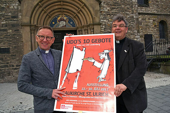 Domkapitular Benedikt Fischer und Monsignore Georg Austen (rechts) präsentieren das Plakat zur Ausstellung „Udos 10 Gebote“, die zu Libori in der Paderborner Gaukirche gezeigt wird. Foto: Patrick Kleibold