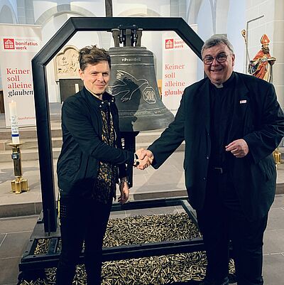 Der Künstler und Sänger Michael Patrick Kelly und Monsignore Georg Austen stehen vor der #PeaceBell, die während des Libori-Festes in der Paderborner Gaukirche ausgestellt wurde. (Foto: Theresa Meier)