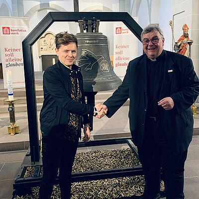 Der Künstler und Sänger Michael Patrick Kelly und Monsignore Georg Austen stehen vor der #PeaceBell, die während des Libori-Festes in der Paderborner Gaukirche ausgestellt wurde. (Foto: Theresa Meier)
