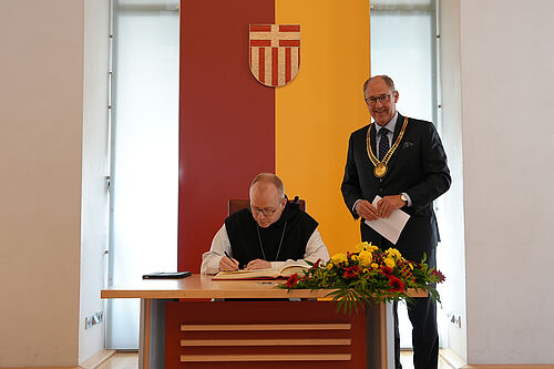 Bischof Erik Varden OSCO (Prälatur Trondheim), Vorsitzender der Nordischen Bischofskonferenz, trägt sich im Beisein von Paderborns Bürgermeister Stefan-Oliver Strate ins Goldene Buch der Stadt Paderborn ein. Foto: Marcus Thielking