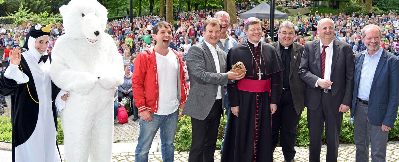 Zum Aktionstag „Tiere der Bibel“ im Karlsruher Zoo kamen über 3.000 Besucher, darunter 2.500 Erstkommunionkinder aus dem gesamten Erzbistum Freiburg. Eröffnet wurde die Veranstaltung auf der Seebühne mit einem gemeinsamen Gottesdienst. Von Links: Pinguin und Eisbär, Moderator Juri Tetzlaff, Zoodirektor Dr. Matthias Reinschmidt, Musiker Reinhardt Horn, Erzbischof Stephan Burger, Monsignore Georg Austen, Bürgermeister Michael Obert und der stellvertretende Zoodirektor Clemens Becker. Foto: Patrick Kleibold