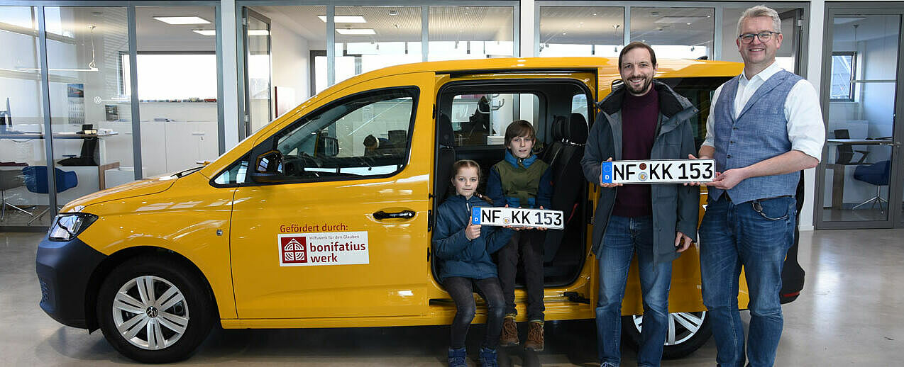 Johanna, Jakob und Christoph Mainka freuen sich über den BONI-Bus, der ihnen von Thomas Twents, Ansprechpartner für die Verkehrshilfe des Bonifatiuswerkes, überreicht wird. (Foto: Simon Helmers)