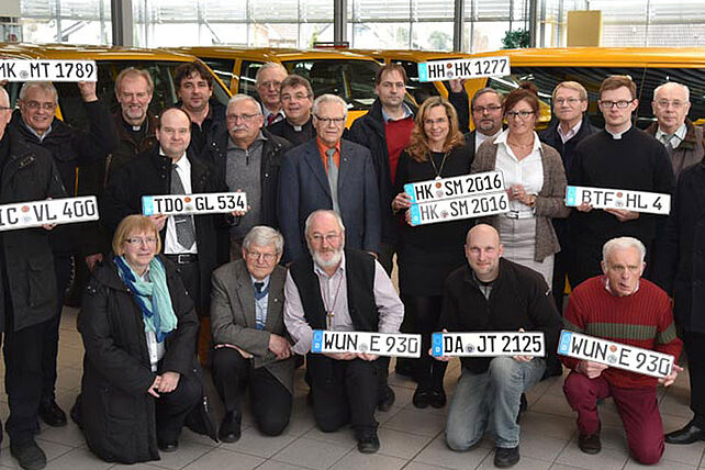 Monsignore Georg Austen (hintere Reihe, 8.v.l.) übergab in Paderborn an die Vertreter von acht Kirchengemeinden und Institutionen aus den Bistümern Erfurt, Essen, Hildesheim, Magdeburg, Mainz und Regensburg und dem Erzbistum Hamburg einen rapsgelben BONI-Bus. Foto: Lena Reiher