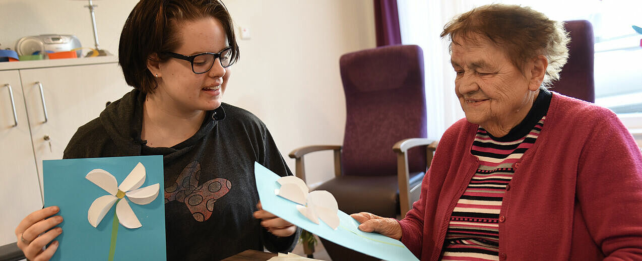 Freuen sich über das Ergebnis: Die 16-jährige Freya aus Berlin-Marzahn hat gemeinsam mit der 90-jährigen Besucherin der Tagespflege im St. Johannisstift ein Blumenbild gebastelt. (Foto: Theresa Meier)