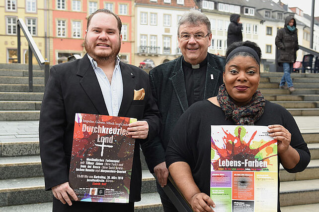 Juan Del Bosco (links), Tiffany Abban und Monsignore Georg Austen präsentieren die Plakate zum Programm für die Kar- und Ostertage in Fürstenberg, Büren, Leiberg und Paderborn. Foto: Sr. Theresita