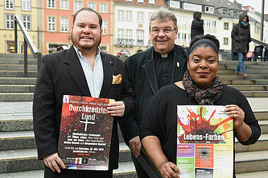 Juan Del Bosco (links), Tiffany Abban und Monsignore Georg Austen präsentieren die Plakate zum Programm für die Kar- und Ostertage in Fürstenberg, Büren, Leiberg und Paderborn. Foto: Sr. Theresita