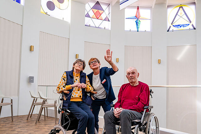 Bettina Hünermund, Leiterin des Caritashospizes Mutter Teresa, zeigt zwei Gästen die bunten Fenster im Raum der Stille. (Foto: Caritas Bistum Erfurt /F. Kalbe)