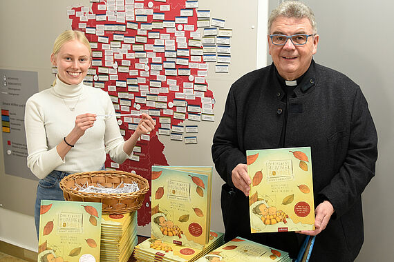 Msgr. Georg Austen, Generalsekretär des Bonifatiuswerkes, mit der Bundesfreiwilligendienstlerin, Greta Boß, während der Verlosung. Im Hintergrund die Deutschlandkarte u.a. mit den geförderten Kitas. (Foto: S. Helmers)