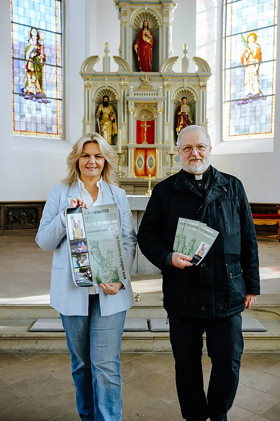 Nina-Maria Mehring und Pastor Stefan Stratmann in der Pfarrkirche St. Cyriakus mit Plakaten und Flyern für die Mysterienspiele in Kleinenberg. Foto: Sonja Funke / Erzbistum Paderborn