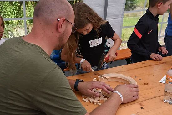 Unter dem wachsamen Blick von Thomas Rhode schlägt Hanna vorsichtig mit einem Hammer und einem Messer kleine Tau-Anhänger aus einem Holzring. (Foto: Simon Helmers)