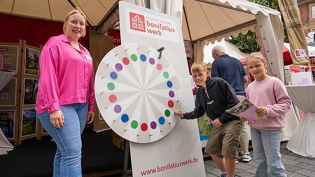 Am Infostand des Bonifatiuswerkes: Leo (10) aus Paderborn hängt sich beim Glücksrad voll rein. Mit im Bild: seine Schwester Leni (7) und Alena Lorenz, ehemalige Freiwillige des "Praktikums im Norden". Foto: Hartmut Salzmann