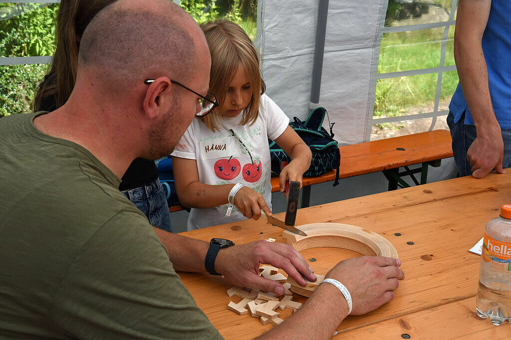 Unter dem wachsamen Blick von Thomas Rhode schlägt Hanna vorsichtig mit einem Hammer und einem Messer kleine Tau-Anhänger aus einem Holzring. (Foto: Simon Helmers)