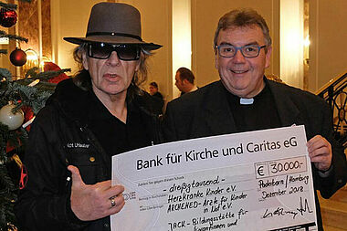 Udo Lindenberg und Monsignore Georg Austen präsentieren den Scheck in Höhe von 30.000 Euro, der an drei soziale Projekte für Frauen und Kinder übergeben wird. Foto: Bonifatiuswerk