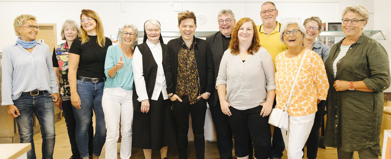 Michael Patrick Kelly bedankt sich gemeinsam mit Monsignore Georg Austen (beide Bildmitte) bei den ehrenamtlichen Helferinnen und Helfern der „PaderMahlZeit“, die Bedürftige unter anderem mit warmen Mahlzeiten versorgen. (Foto: Julia Carola Pohle)