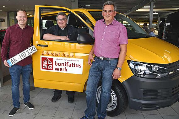 Jeffrey Merker (links) und Christoph Stinne (rechts) erhalten den neuen BONI-Bus von Msgr. Georg Austen. (Foto: Sr. Theresita M. Müller)
