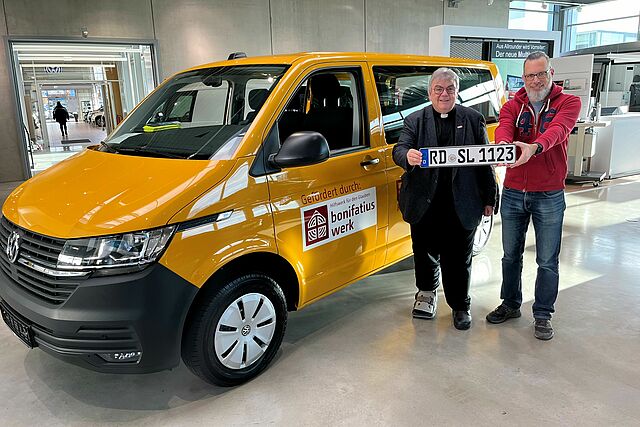 Monsignore Georg Austen, Generalsekretär des Bonifatiuswerkes, übergibt den neuen Bonibus an Alexander Hausch, Verwaltungskoordinator der Pfarrei St. Ansgar in Rendsburg im Erzbistum Hamburg. Foto: Bonifatiuswerk/Marius Thöne