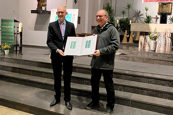 Dominique Lagast, Referent im Finanzministerium für Postwertzeichen, zeigt gemeinsam mit Pater Kalle Lenz der St.-Christophorus-Gemeinde die grüne Weihnachtsbriefmarke. (Foto: Erzbistum Berlin)